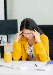Woman at work sitting at a desk with head in hands needing support with mental health crises in the workplace
