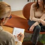 Female sitting on chair across from female therapist who is taking notes as they talk