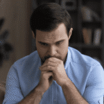 Man sitting on couch with chin resting on his hands worrying about memory processing in PTSD