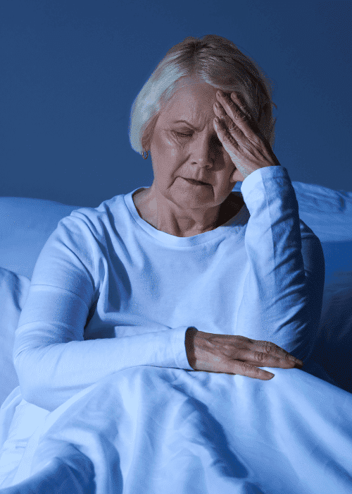 Woman sitting up in bed with hand on forehead worrying about chronic stress and the brain