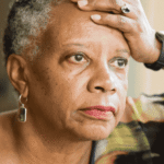 Woman sitting with hand on head looking out window wondering about lifestyle psychiatry approach to mental health