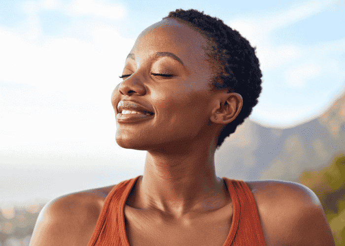 Woman standing outside in nature with eyes closed smiling after support with memory processing in PTSD