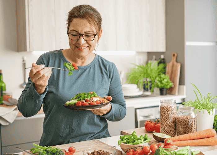 Woman in kitchen eating healthy meal and smiling after support with blood sugar and anxiety