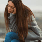 Woman sitting outside on low wall with head resting on hand needing support with epigenetics and trauma