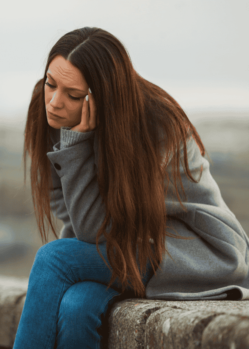 Woman sitting outside on low wall with head resting on hand needing support with epigenetics and trauma