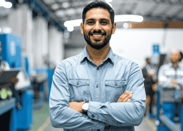 Man standing in factory with arms crossed smiling after receiving support with epigenetics and trauma