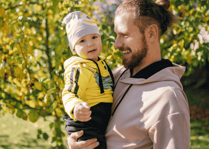 Man outside in sunshine at the park holding baby son after support with sunlight and mood regulation