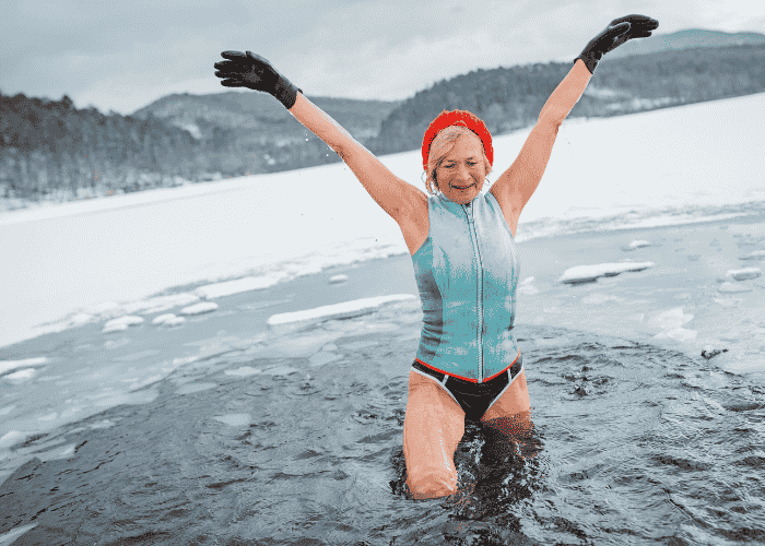 Woman outside in ice plunge celebrating and smiling with arms in the air after researching cold exposure and mental health
