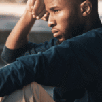 Man sitting on step outside with knees drawn to chest and head resting on hand needing support with longevity psychiatry