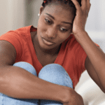 Woman holding her knees into her chest with one hand and resting her head on the other hand looking worried