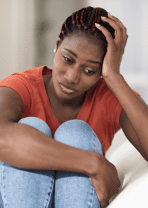 Woman holding her knees into her chest with one hand and resting her head on the other hand looking worried