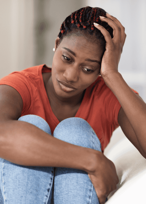 Woman holding her knees into her chest with one hand and resting her head on the other hand looking worried