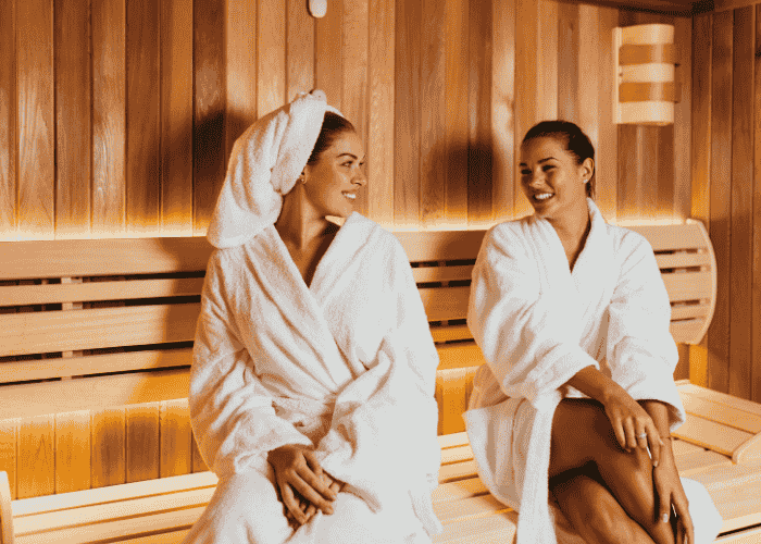 Two women sitting in sauna smiling after researching sauna therapy and mental health