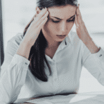 Woman sitting at desk looking at paperwork with head in hands worrying about single case agreement info for out-of-network insurance for mental health care