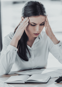 Woman sitting at desk looking at paperwork with head in hands worrying