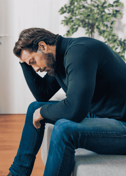 Man sitting on couch with head resting on hand worrying about serotonin and depression