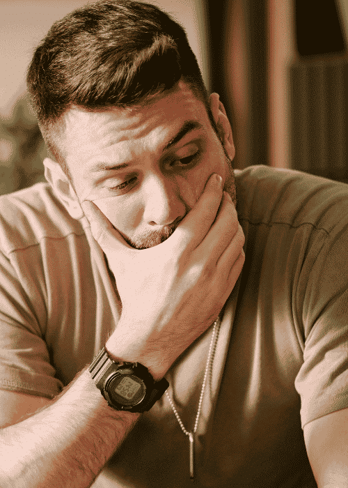 Man sitting on couch with hand over mouth needing support with how trauma affects the nervous system.