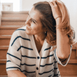 Woman sitting on stairs moving her hair back from her face needing support with perimenopause and mental health