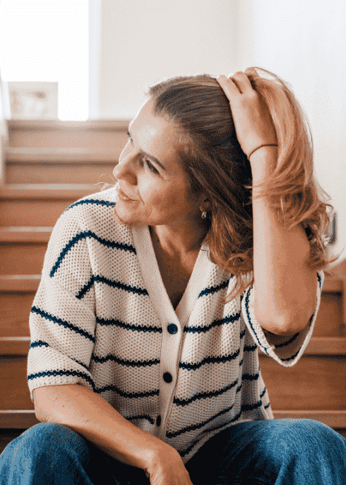 Woman sitting on stairs moving her hair back from her face needing support with perimenopause and mental health