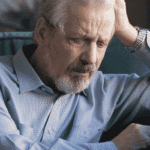 Man sitting on couch with head in hand in need of neuropsychological assessments