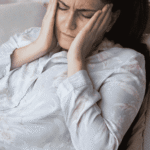 Woman sitting on couch with hands on face needing support with the psychological effects of chronic illness
