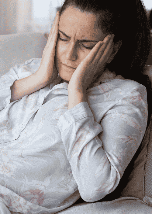 Woman sitting on couch with hands on face needing support with chronic illness and mental health