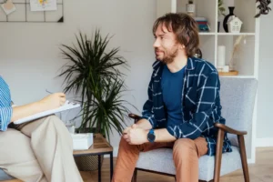 Man with beard sitting in a chair talking to a therapist during outpatient mental health treatment