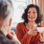 Woman sitting on couch with friends holding a cup of tea and smiling after support with perimenopause and mental health