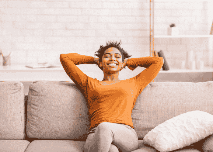 Woman sitting on couch with hands behind head and legs crossed smiling after support with hormonal cycles and depression