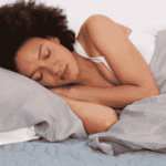 Woman sleeping soundly on grey pillow with hands tucked under her head and covered with bedding after support with sleep architecture and mental health