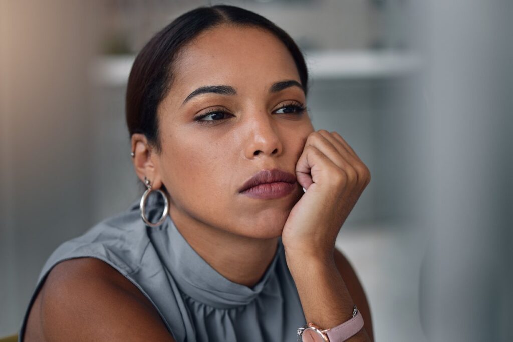 Woman with serious look on her face staring off into the distance as she leans her chin on her hand