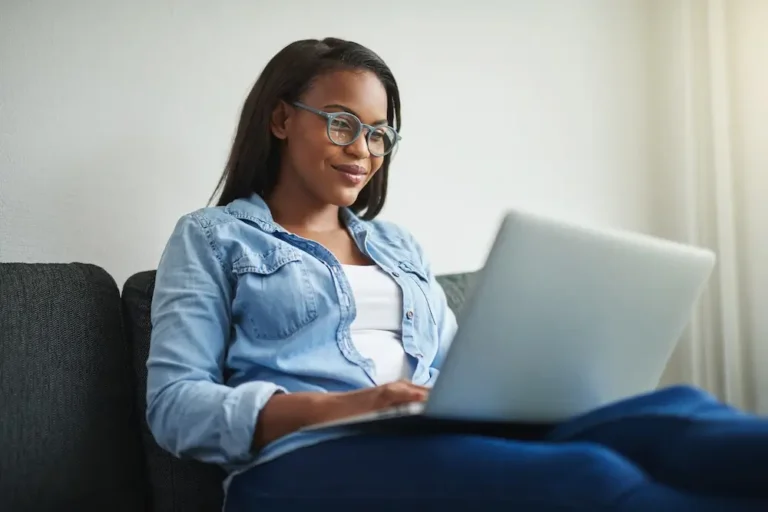 Woman sitting on couch looking at laptop during virtual outpatient therapy session for mental health