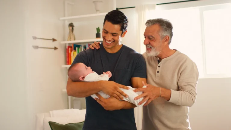 Newborn baby being held by his father with his grandfather standing near